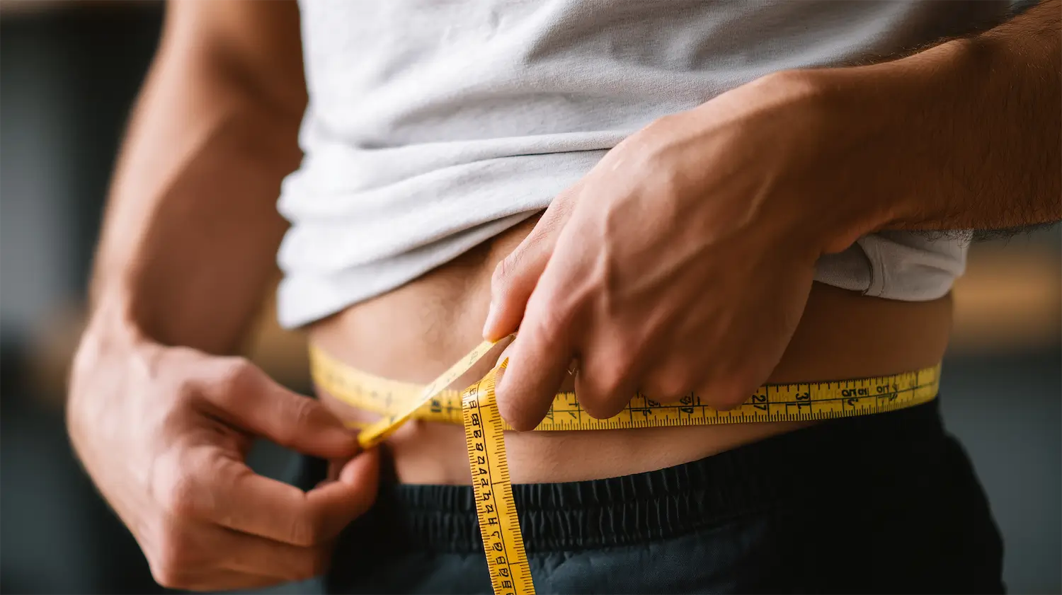 Man measuring himself for a suit at home with a tape measure